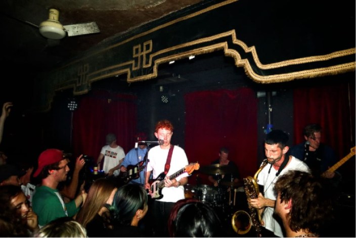 King Krule and band playing a small room under red curtains