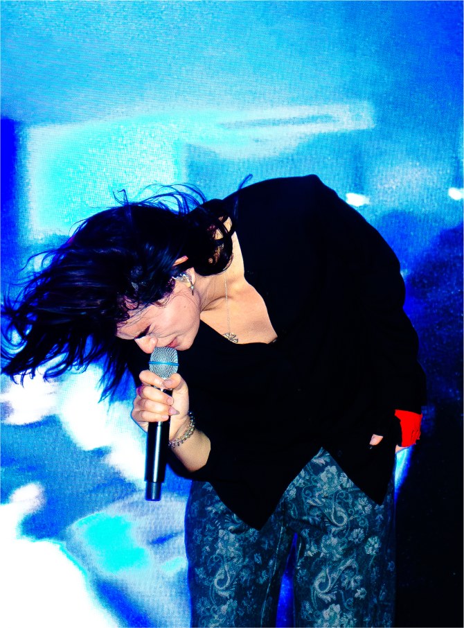 Underscores performing, hair flying, lit in electric blue